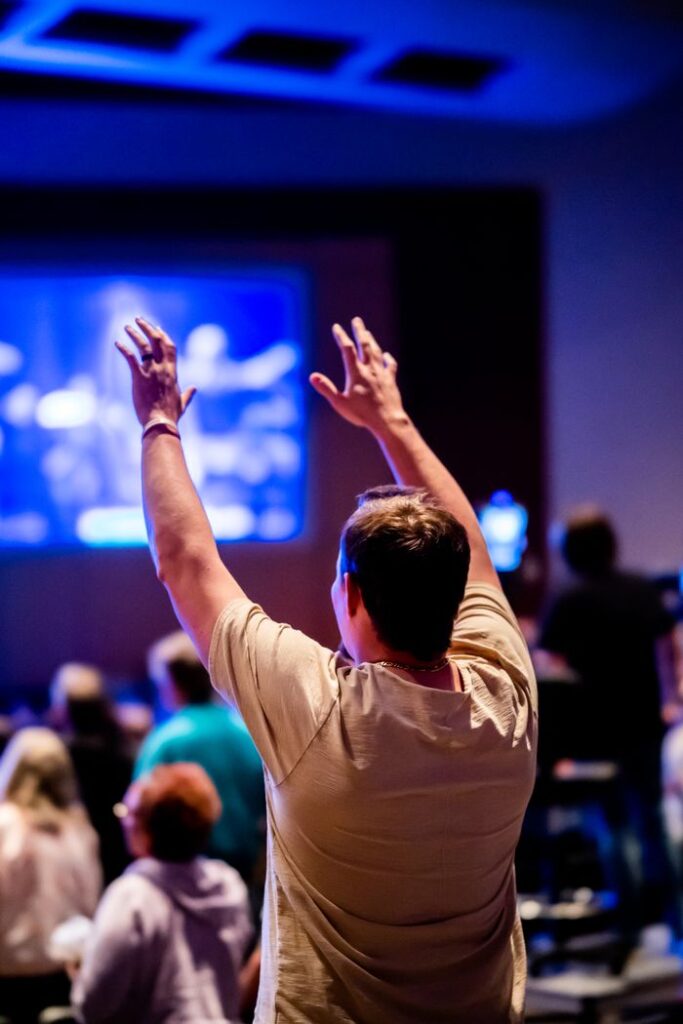 A man raises his hands in worship during an indoor religious gathering.