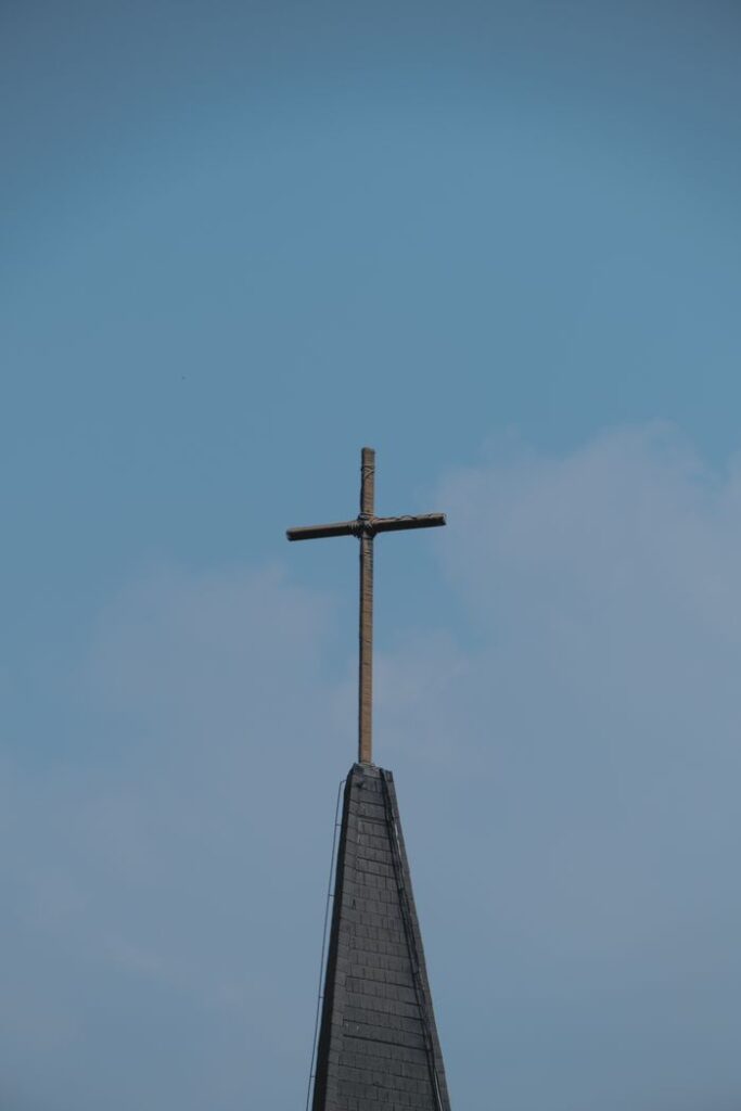 A cross atop a church steeple against a clear blue sky, symbolizing faith and spirituality.